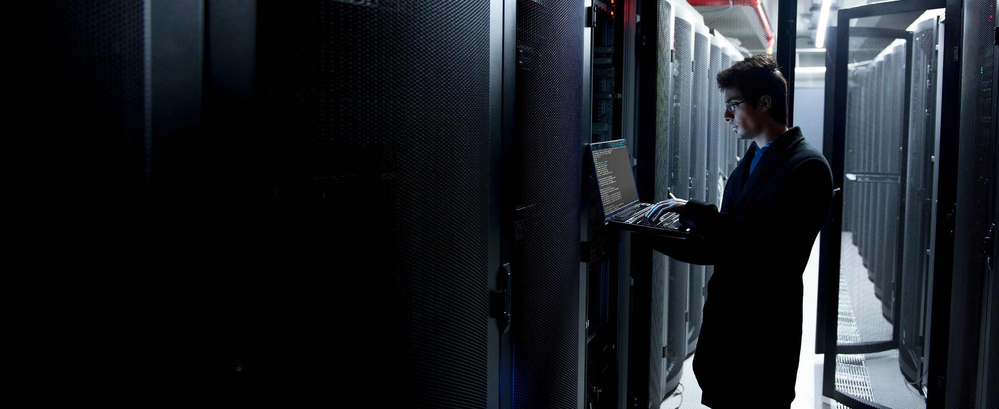 IT worker in enterprise data center working on the network via a laptop