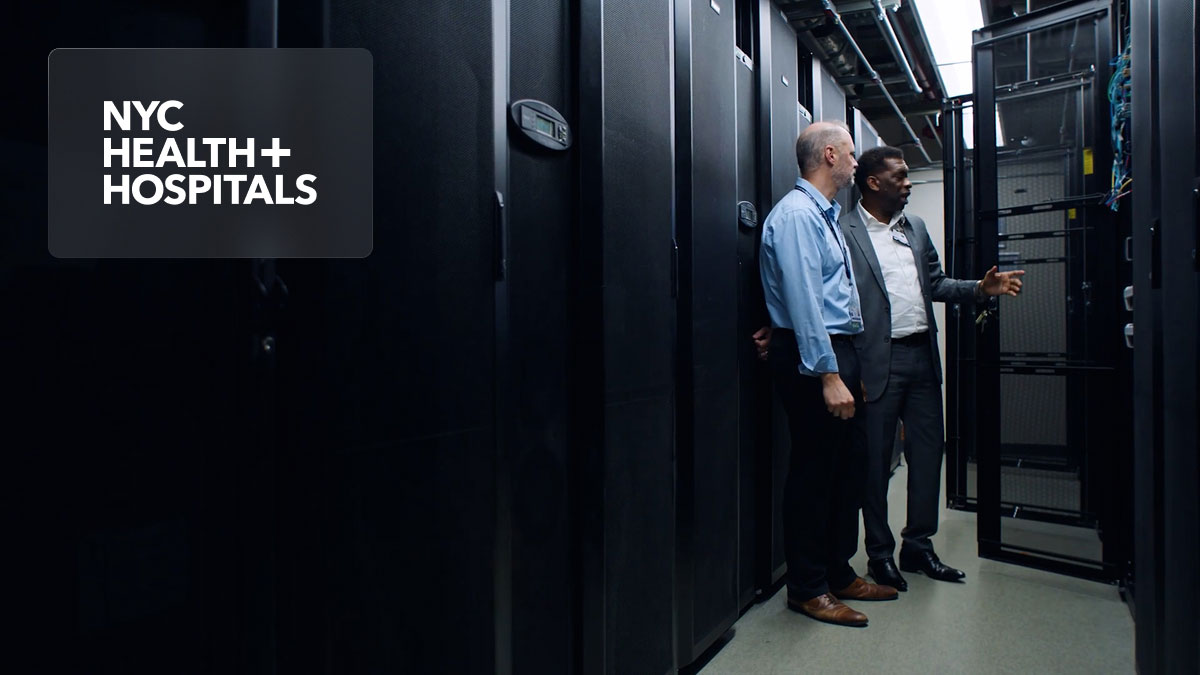 NYC Health + Hospitals logo; two men in a data center reviewing server racks