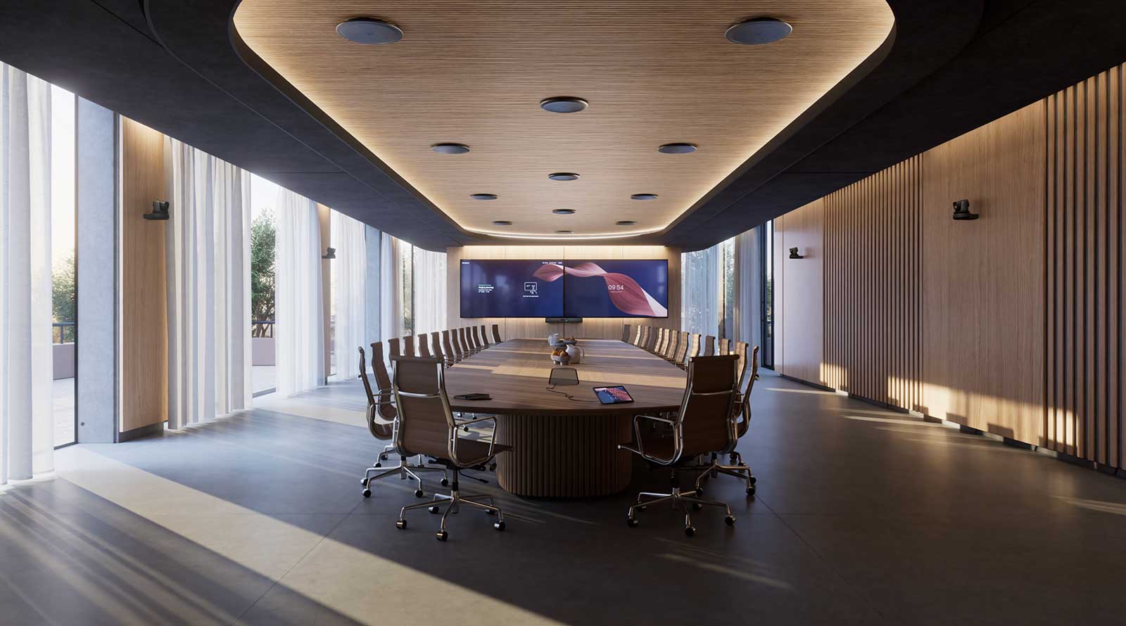 Modern boardroom with a long table, leather chairs, wall mounted cameras, ceiling microphones, and a screen showing a four-person video conference call.